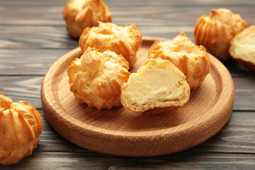 Homemade profiteroles with cream on wooden plate on brown background. Fresh baked golden profiterole.