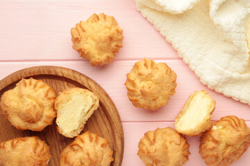 Homemade profiteroles with cream on wooden plate on pink background. Fresh baked golden profiterole.
