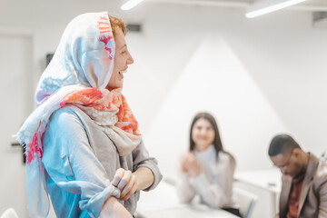 Redhead muslim businesswoman giving presentation speech to a multiracial group of businesspeople. Ginger businesswoman wearing hijab listening to a colleague and smiling