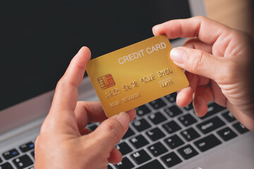 Woman's hand holding a credit card with a computer in the back.