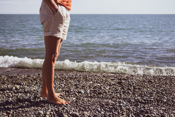 Bare feet of a girl in shorts on a pebble beach by the sea on a sunny day, toned. Vacation...