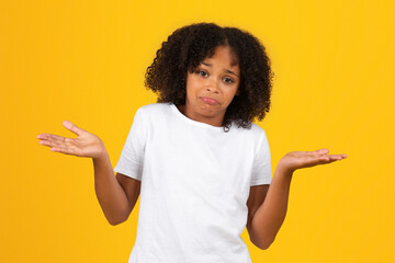 Confused funny stupid adolescent african american girl in white t-shirt, spreads arms to sides,...