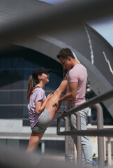 Side view shot of fit, handsome male person helping his flexible female friend stretching her legs before training. She is talking to him and laughing