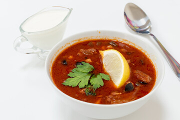 Appetizing tomato soup with meat, greens and slice of lemon in white plate on white background