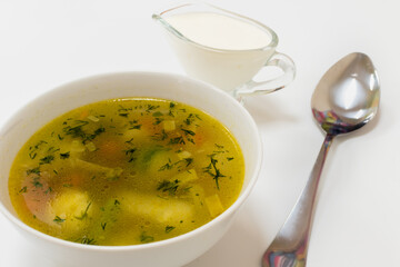 Appetizing soup with chicken balls, herbs and carrot and potatoes in white plate on white background