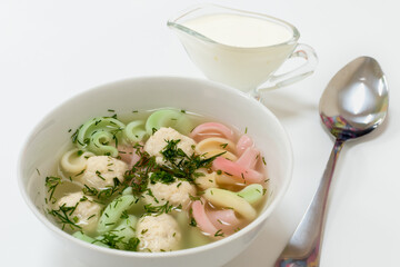 Appetizing light soup with chicken balls, herbs and colored pasta in white plate on white background