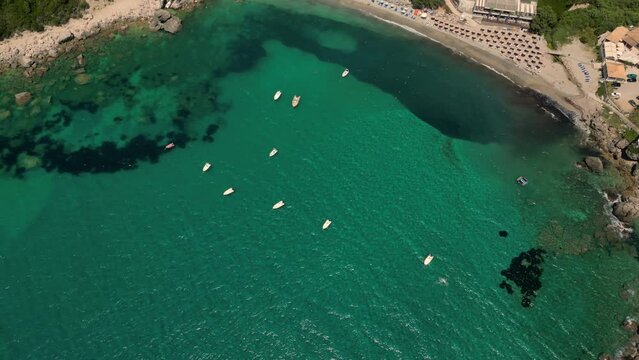 Drone footage of boats gently swaying in the sunny sea, moored not far from the Paralia Ermones Beach, on a hot day