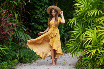 Young woman in a stylish summer dress enjoys the beauty of a tropical resort, walking among palm trees and embracing the vacation vibes. Concept of travel and summer relaxation.