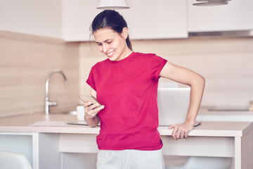 A young woman checks social networks while holding a smartphone at home. A smiling woman uses a mobile phone app, plays games, makes purchases online, orders delivery. High quality photo