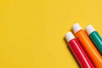 THREE TUBES OF SCHOOL PAINT, ON A YELLOW BACKGROUND.