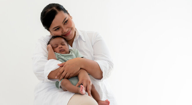 Portrait image an Asian mother happy and smile while holding a 1-month-old baby newborn son who is sleeping happily on his mother's chest, to relationship in family and baby newborn concept.