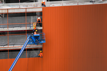 workers install material of metal wall on facade structure building. The construction of modern hi...