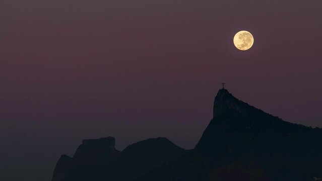 Rio de Janeiro, Brazil - June 4, 2023: Time lapse video of full moon setting behind Corcovado mountain with Christ the Redeemer statue on top of it.