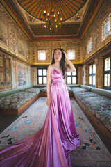 a beautiful girl in a long pink dress poses in a room with a traditional Turkish interior