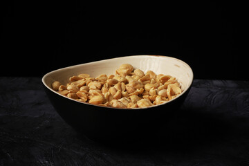 A plate with salted pistachios in a dark room on a dark background. Close-up
