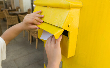 Boy putting a letter in the spanish yellow traditional mailbox
