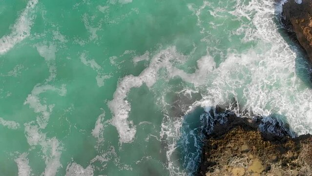Rocks against ocean waves, overhead super slow motion view from drone