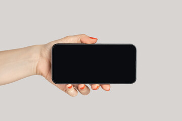 Closeup of woman hand showing mobile phone with blank screen, smartphonewith empty display, advertisement area. Indoor studio shot isolated on gray background.