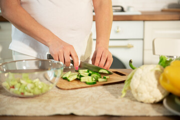 Obraz na płótnie Canvas A pregnant woman cuts vegetables into a salad in the kitchen.