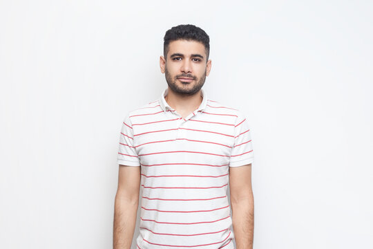 Portrait of calm satisfied delighted bearded man wearing striped t-shirt standing looking at camera, expressing positive emotions. Indoor studio shot isolated on gray background.