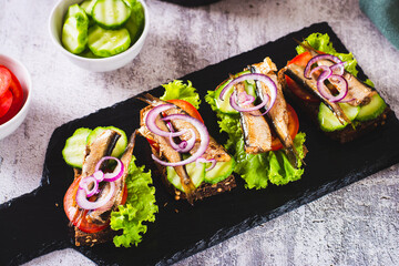 Sandwiches on rye bread with smoked sprats, vegetables and herbs on slate
