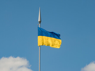 The national flag of Ukraine fluttering in the wind on a high flagpole against the background of the sky and clouds close-up