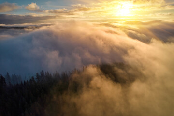 Naklejka na ściany i meble Fog spreads over the mountains at dawn. The sun rises on the horizon. Carpathians in the morning. Aerial drone view.