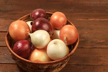 Various varieties of onions in a basket on a wooden background, autumn harvest concept, red, white and golden onions for breeding in agriculture, selective focus