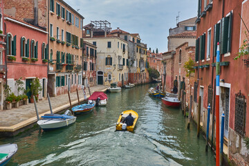 Fototapeta na wymiar Old canal with bridge, gondola, houses, flowers in cloudy weather. Venice