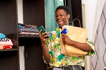 african man using Smartphone and credit card standing in mall holding shopping bag