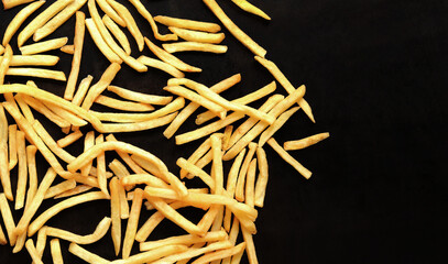 Fried sliced potatoes on a dark background, top view. French fries scattered on a wooden table. Fast food. Cover for the menu