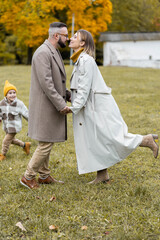 Fototapeta premium Happy family on a beautiful fall picnic in the park. Cozy autumn vibes. Young father, mother and their cute sn spending quality time together, having fun.
