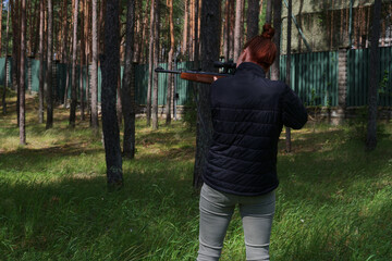 Young redhead woman protecting her house or on tactical gun training classes. Woman with weapon. Outdoor Shooting Range. Lady with rifle machine gun in the forest