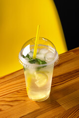ummer refreshing lemonade with mint and ice cubes in a plastic glass with a plastic lid and straw. Dark background, place for text. 