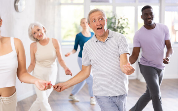 Elderly retired man and students of different ages is actively moving at modern dance and aerobics lesson in fitness room. Hobby, healthy lifestyle concept