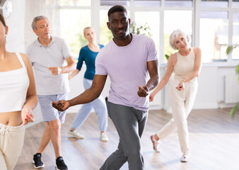 Fototapeta premium African American man is engaged in modern dance class with group friends of different age and learn to perform movements to rhythmic music.