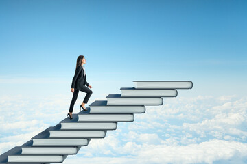 Side view of young businesswoman climbing book steps on bright blue sky with clouds background....