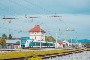 Passenger train in white and blue  is rushing through the station of Ljubljana Vizmarje on a summer day. Low profile photo, other trains visibile on the station