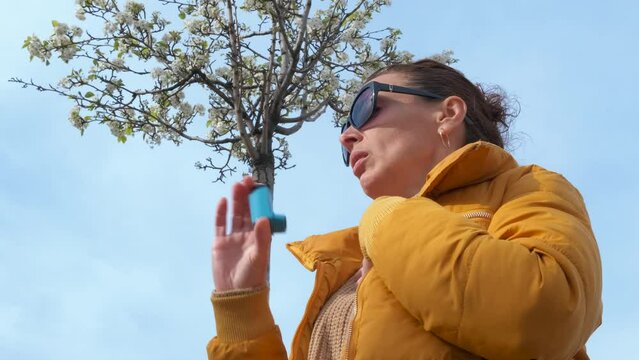 Woman with asthma against sky. A view of sick female use an inhaler against clear blue sky.