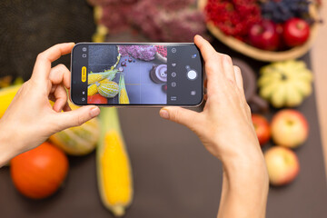 The blogger takes photos and videos on the phone. Hands with phone close-up. A girl shoots a background with an autumn harvest on her phone. Autumn vegetables, fruits, clay brown teapot on a brown
