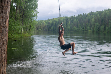 boy jumps into the water using a tarzan swing while swimming in a forest lake