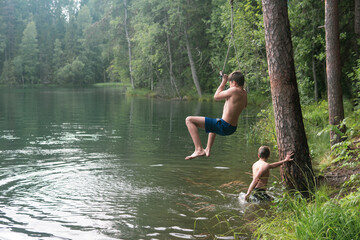 boys jumps into the water using a tarzan swing while swimming in a forest lake