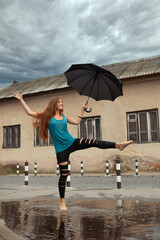 happy young girl with umbrella dancing in a puddle