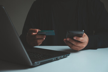shopping online concept. Young adult male hands holding using mobile smartphone and credit card making online payment with laptop computer on table while holiday