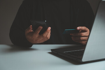 shopping online concept. Young adult male hands holding using mobile smartphone and credit card making online payment with laptop computer on table.