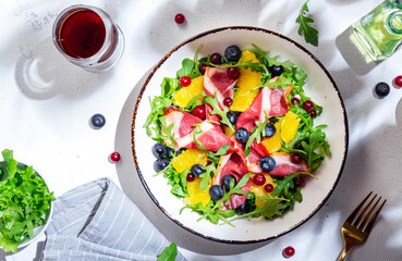 Delicious salad with smoked duck, oranges, blueberries, cranberries and arugula on white table...
