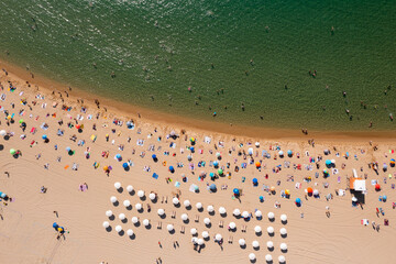 Birds eye view of crouded beach. People lying on sand and swimming in water.