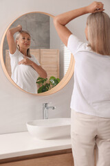 Beautiful senior woman doing breast self-examination near mirror in bathroom