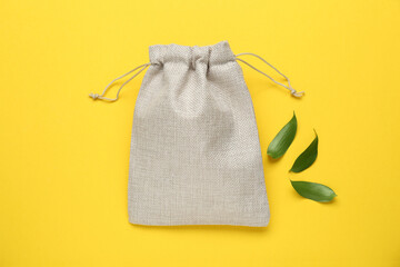 Burlap bag and green leaves on yellow background, flat lay