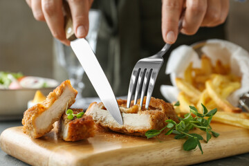 Woman eating delicious schnitzel at grey table, closeup
